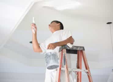 Man on a ladder painting an interior roof