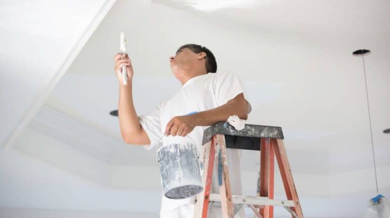 Man on a ladder painting an interior roof